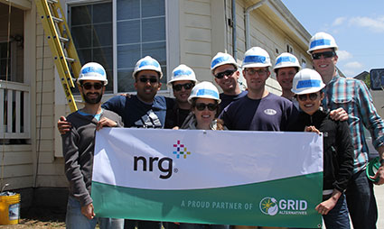 Group of construction workers holding NRG banner in front of house under renovation