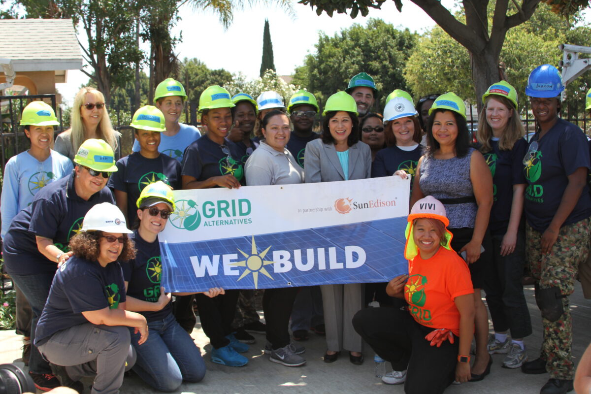Group of people wearing hard hats holding "We Build" banner for GRID Alternatives and SunEdison solar installation event