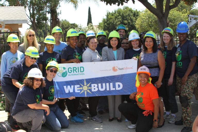 Group of people wearing hard hats holding "We Build" banner for GRID Alternatives and SunEdison solar installation event