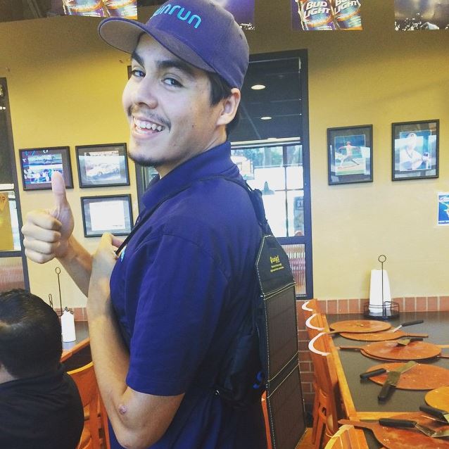 Smiling employee in blue GRID uniform and cap giving thumbs up in restaurant dining area