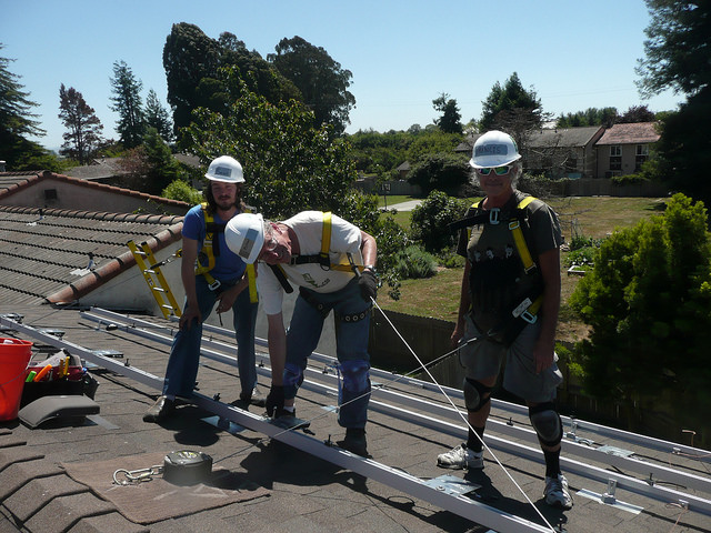 Three workers in safety gear on a residential roof installing solar panels on a sunny day
