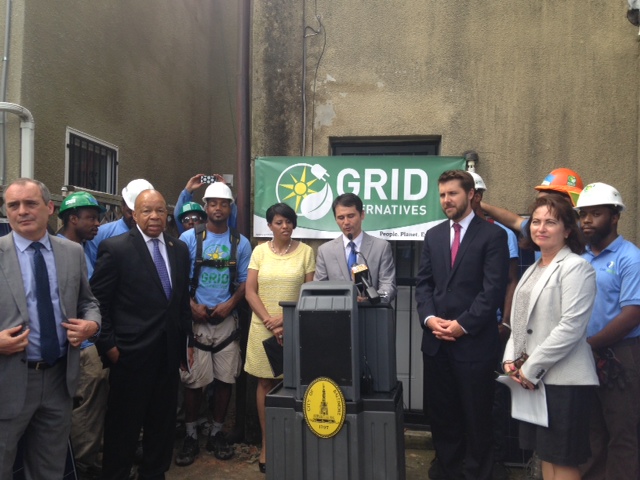 Group of officials and workers at podium with GRID Alternatives banner during solar energy announcement