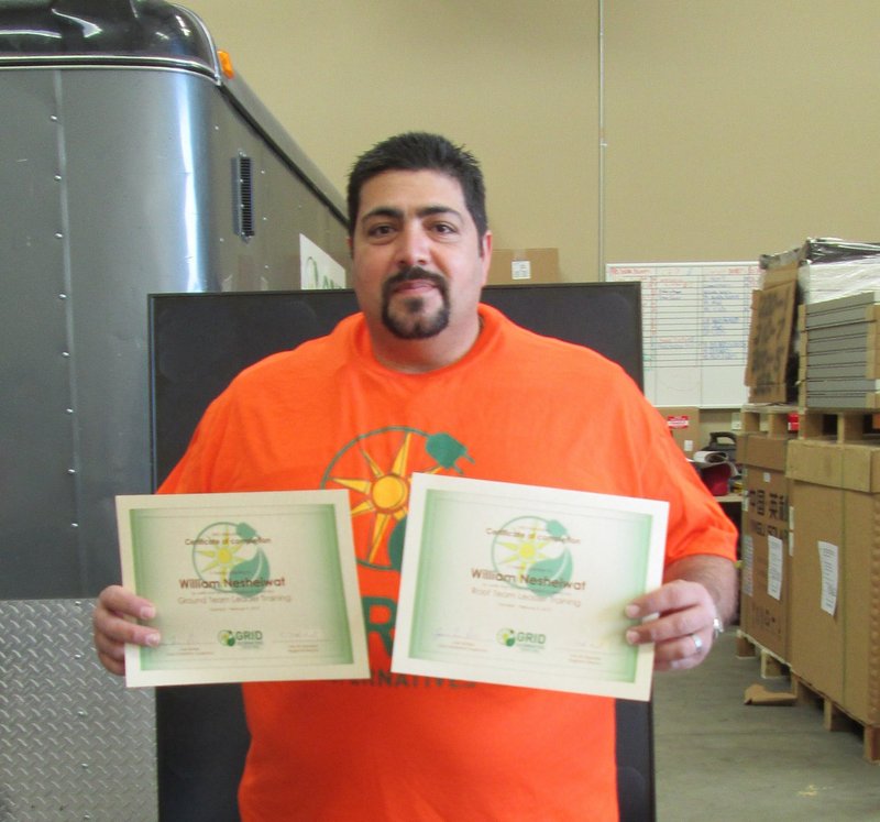 Man in orange shirt holding two solar energy certificates in warehouse setting