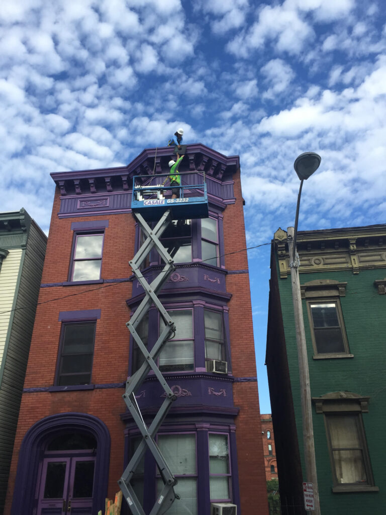 Workers on scissor lift installing energy-efficient equipment on red brick building facade