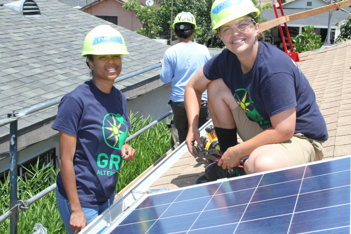 Women in hard hats and safety gear installing solar panels on a residential roof