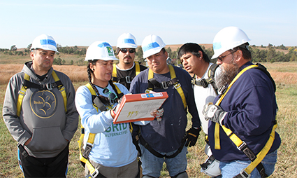 Team members in hard hats and safety vests examine documents in a field during a solar project site visit