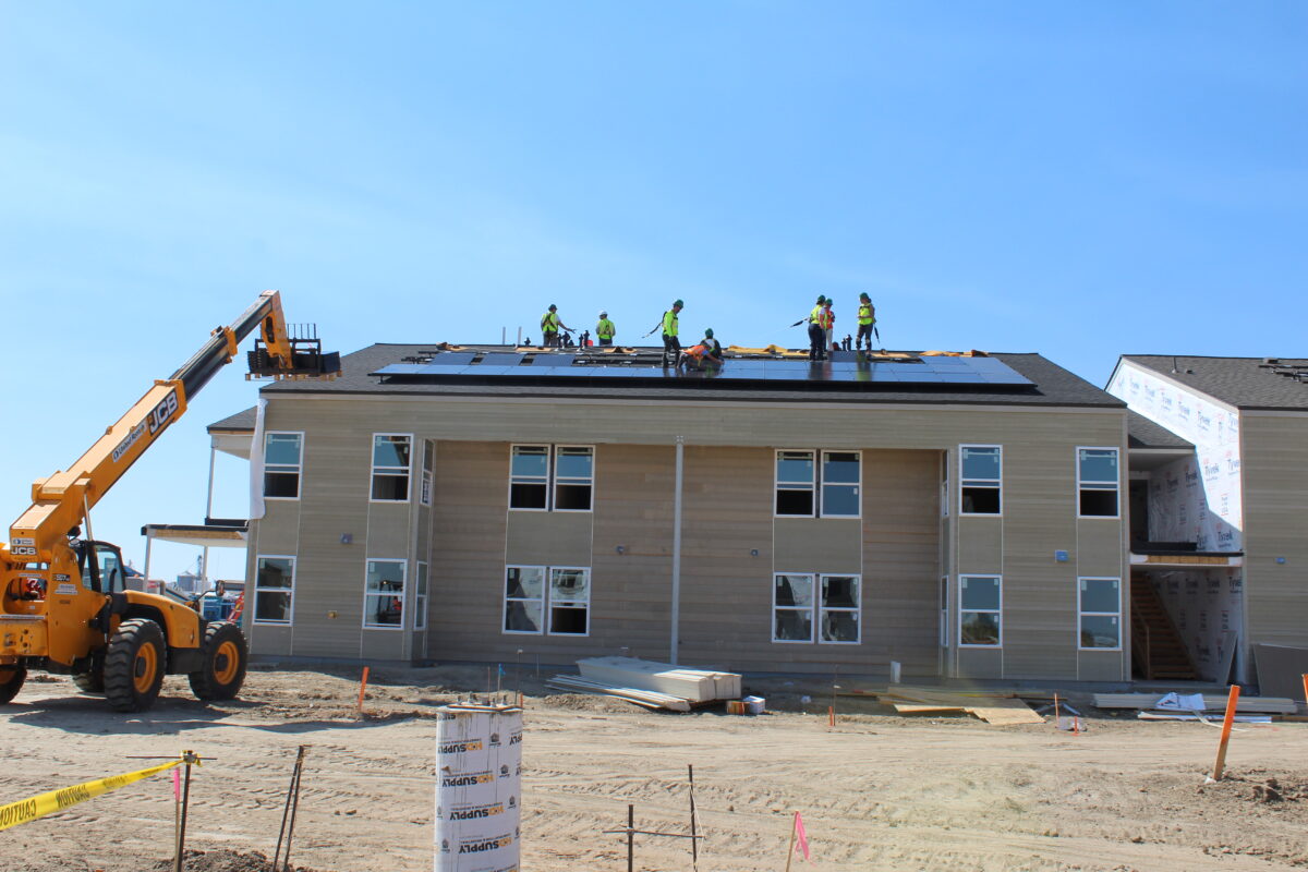 Construction workers install solar panels on roof of residential building under clear blue sky