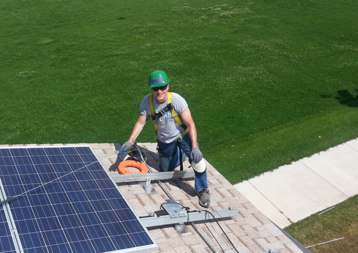 Worker installing solar panels on residential roof while wearing safety gear and helmet