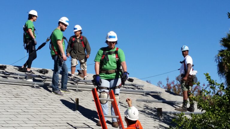 Construction workers in hard hats and safety gear working on a residential roof installation project