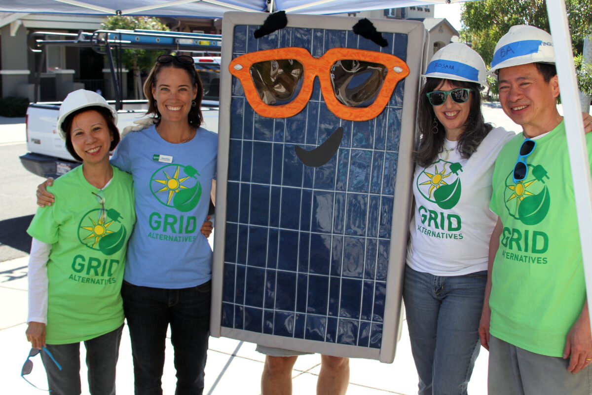 Five GRID Alternatives staff members pose with a large solar panel decorated with a smiling face