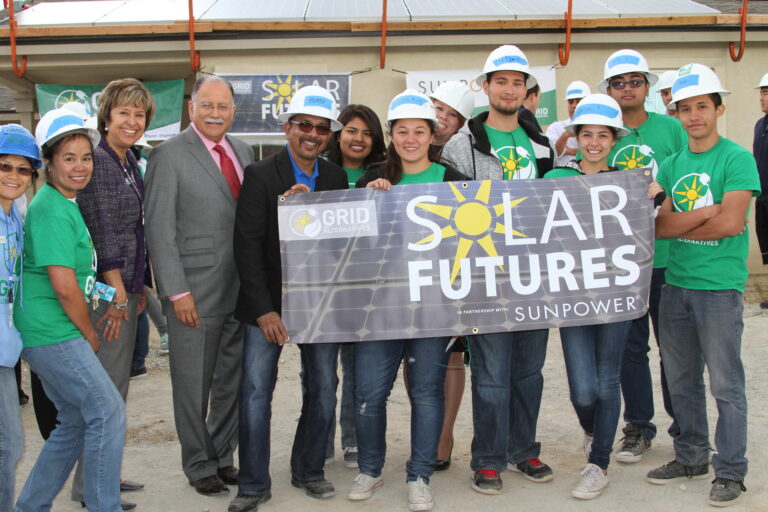 Group of students and officials holding a "Solar Futures" banner with Sunpower logo at a solar installation site