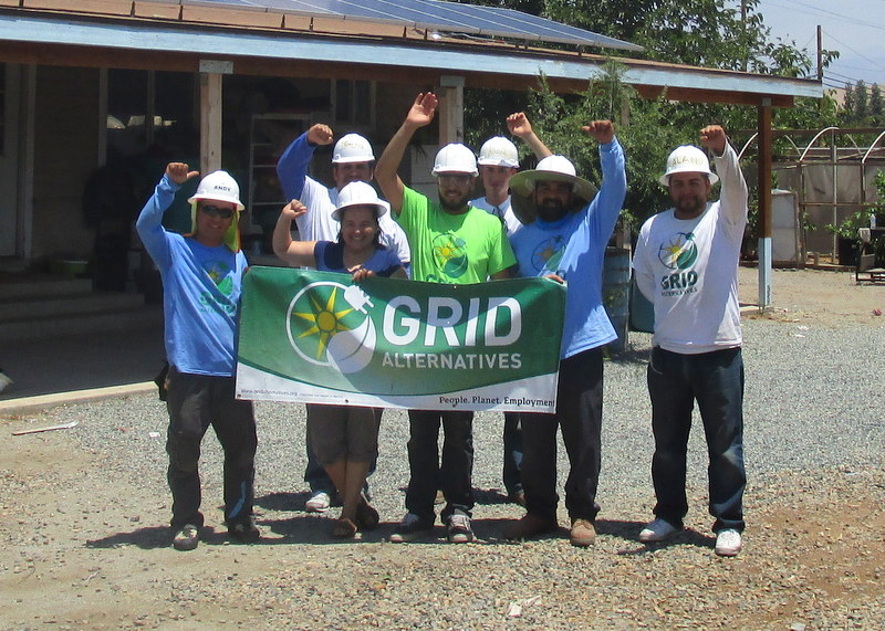 GRID Alternatives team celebrating at a construction site, holding banner with fists raised