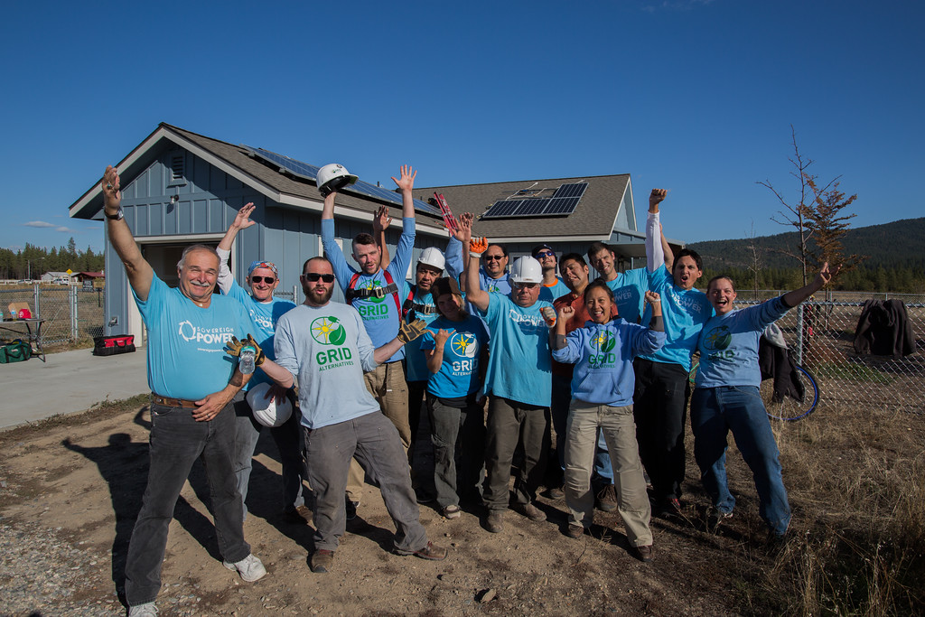 Group of volunteers in blue shirts celebrating in front of a house with solar panels installed