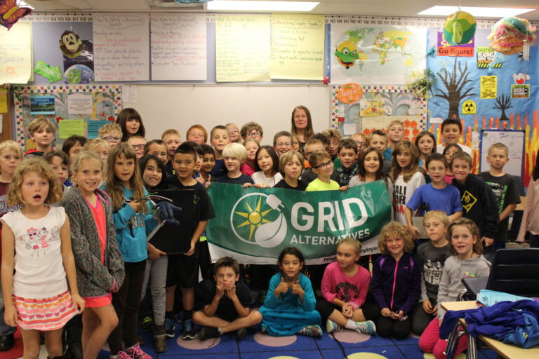 Large group of elementary school students holding GRID Alternatives banner in classroom