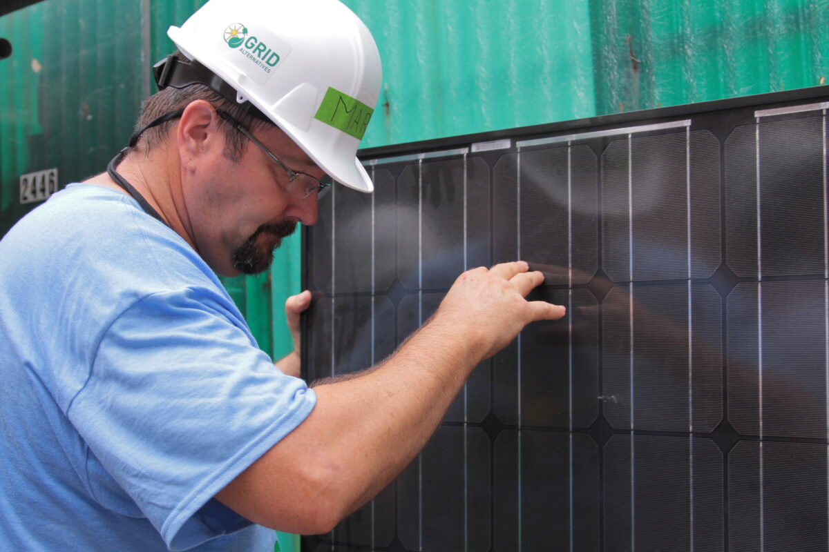 Technician inspecting a solar panel mounted on green container with hard hat and glasses
