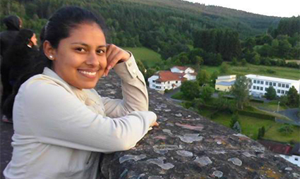 Woman smiling on stone rooftop overlooking green valley with houses and solar panels below