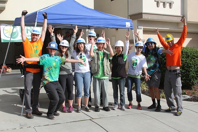 Group of people in hard hats and green shirts cheering under a blue tent at an outdoor event