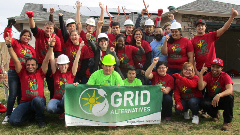 Group of volunteers in red shirts holding GRID Alternatives banner at construction site