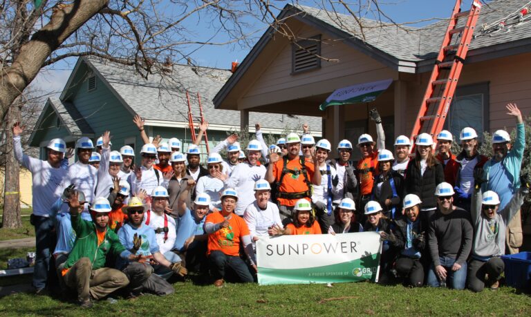 SunPower employees in hard hats pose with banner at residential solar installation in Austin community