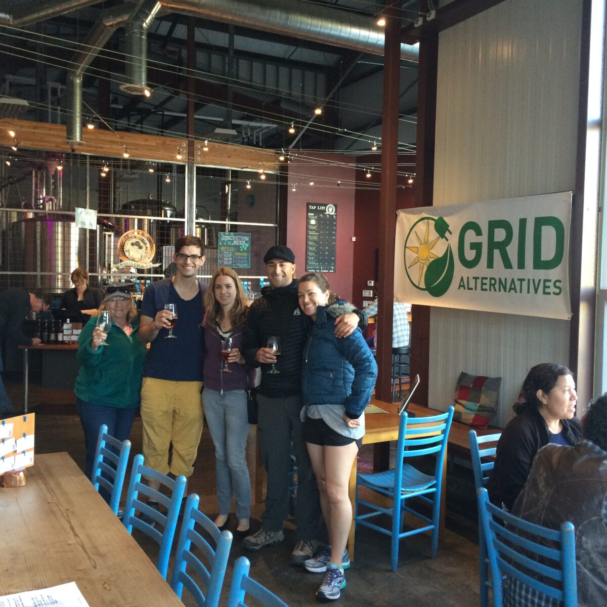 Five people posing together at Discretion Brewery with Grid Alternatives logo visible behind them