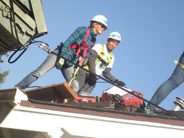 Two workers in hard hats and safety gear installing solar panels on a rooftop under clear blue sky