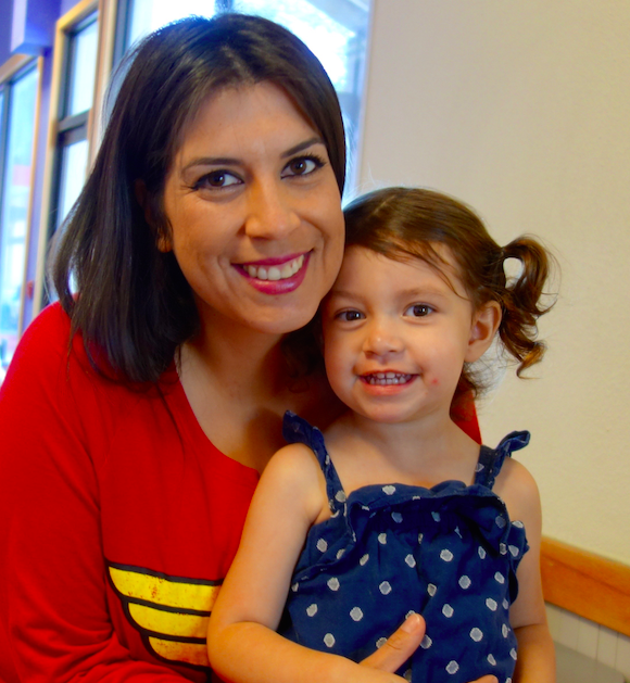 Woman in red shirt holding smiling young child in polka dot dress
