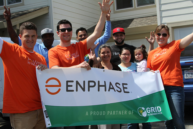 Group of Enphase volunteers in orange shirts holding company banner at community event
