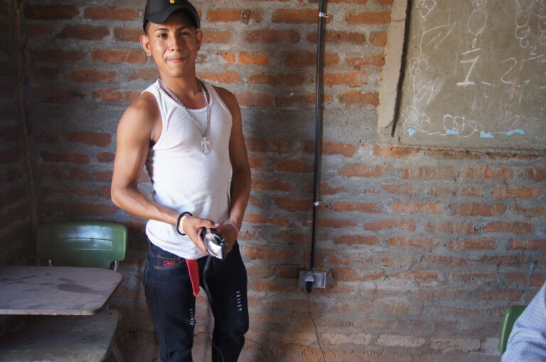 Young man in white tank top and cap standing in brick room, smiling at camera