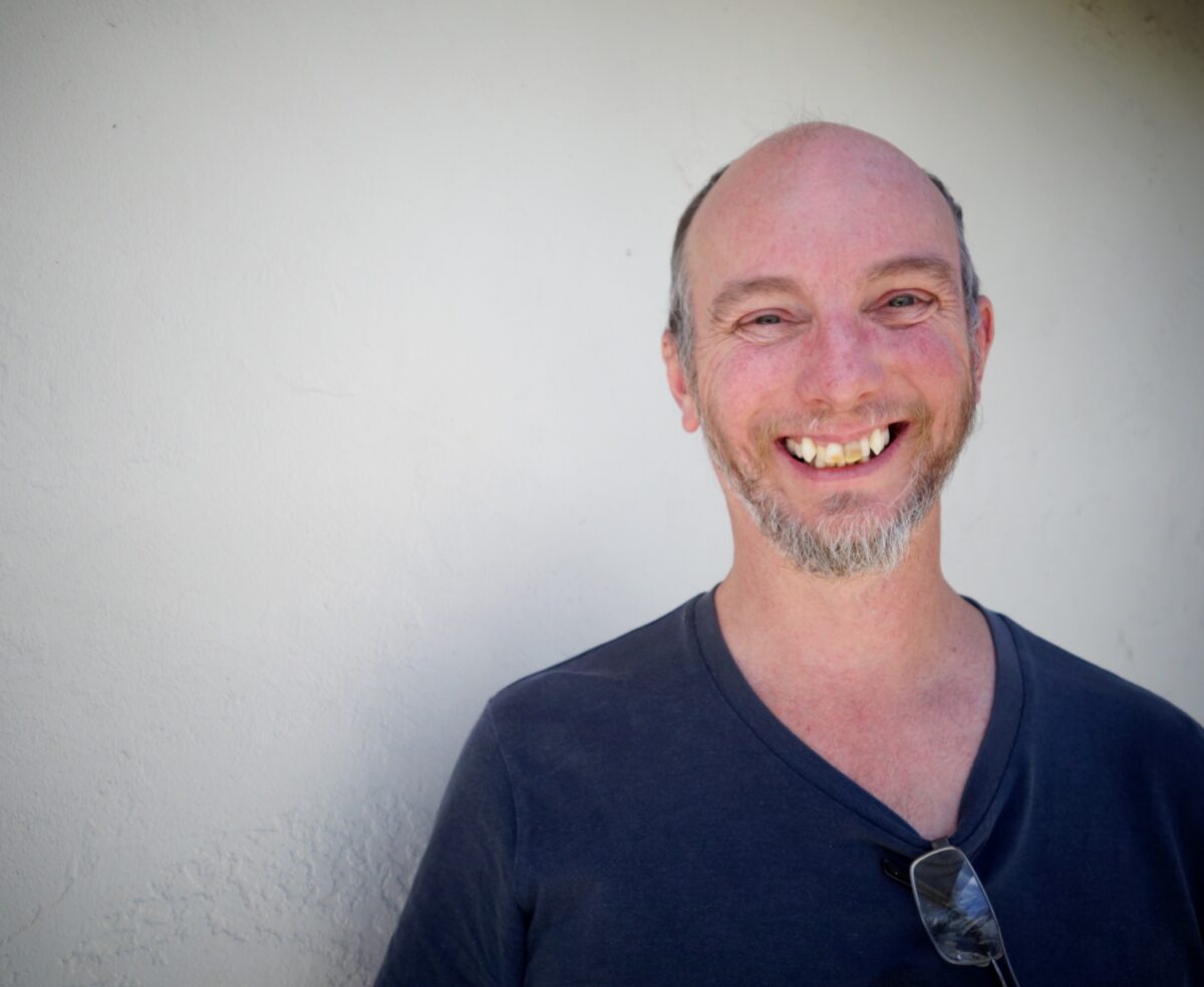 Smiling man with beard wearing dark v-neck shirt against white wall