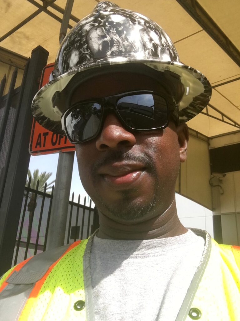 Construction worker in safety helmet and reflective vest wearing sunglasses, smiling outdoors