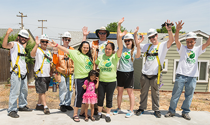 Group of volunteers in green shirts celebrating at a solar installation site with raised arms