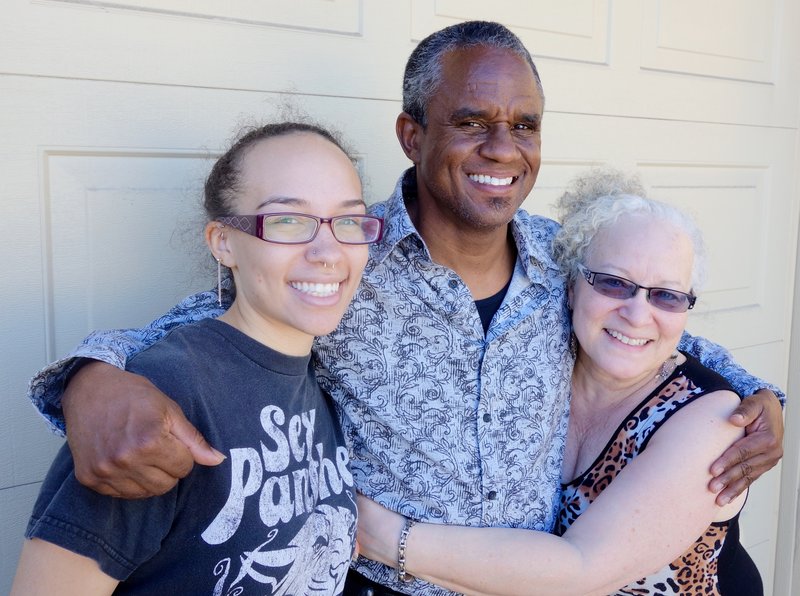 Three smiling people posing together in front of a white garage door, appearing happy and excited