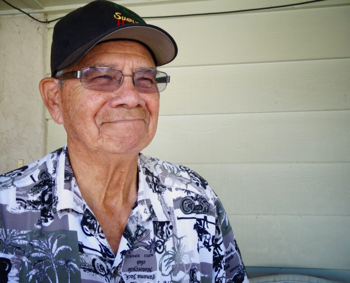 Older man wearing glasses and cap smiles indoors, discussing solar energy concerns