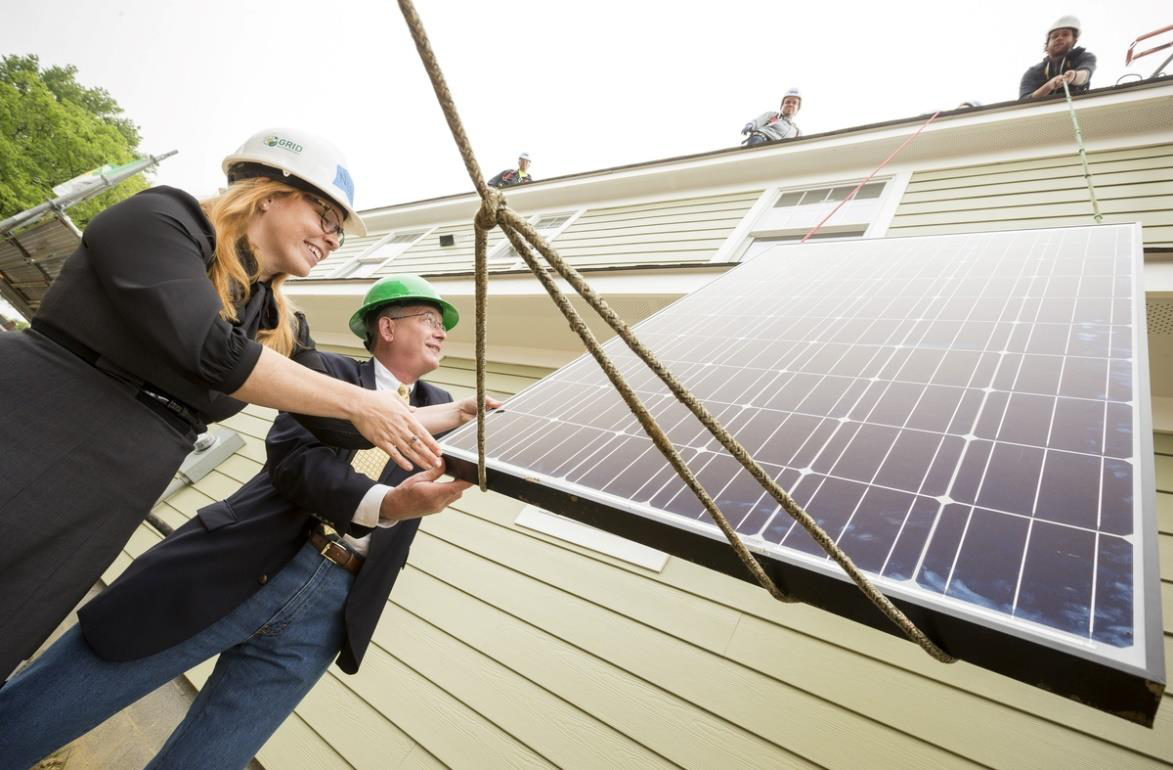 Two professionals in hard hats examine solar panels being installed on a residential roof