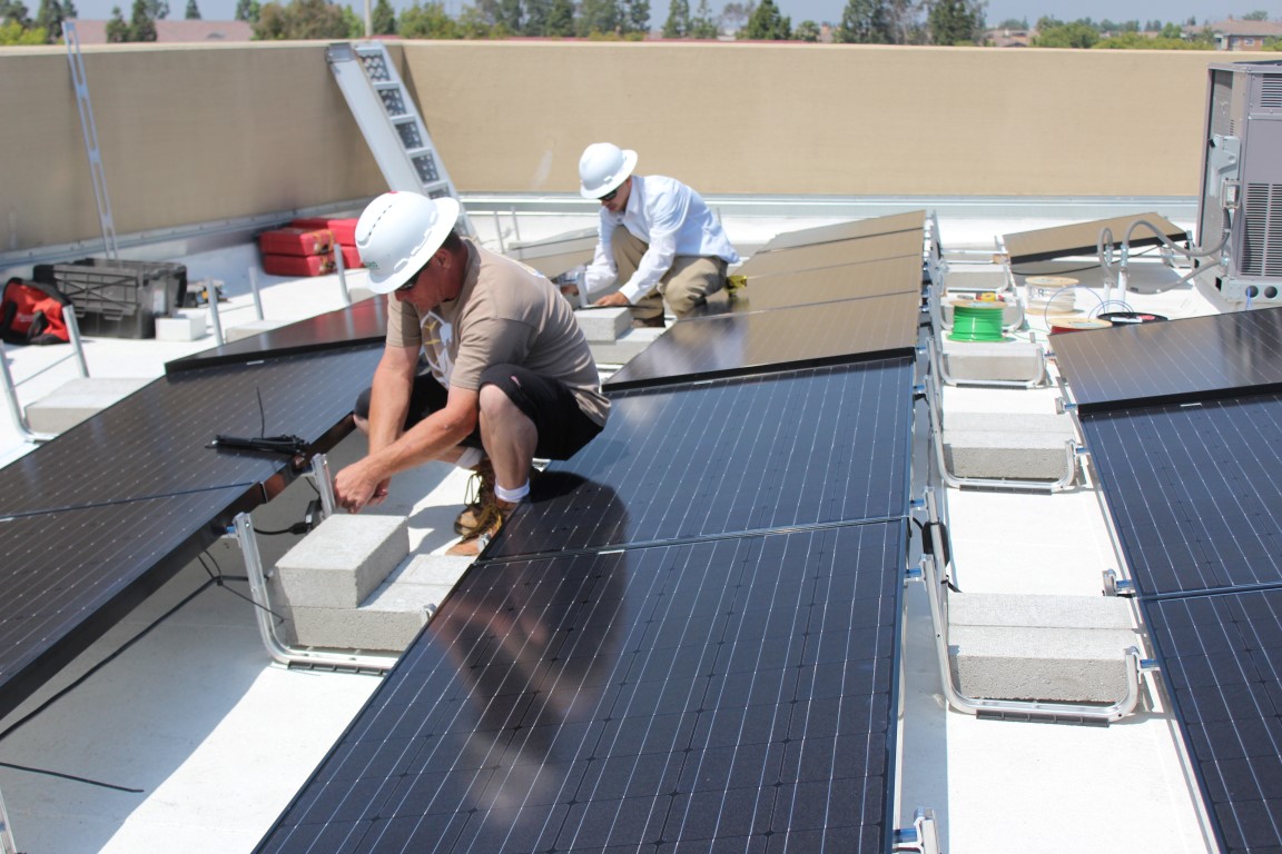 Two workers install solar panels on a commercial rooftop in bright sunlight