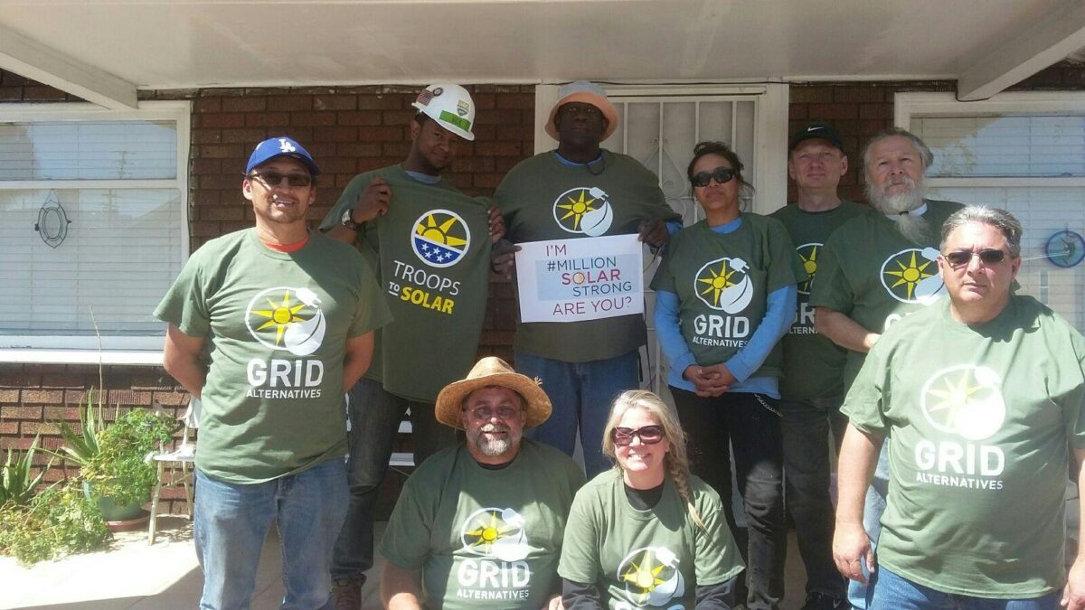 Group of people wearing GRID Alternatives t-shirts posing together outdoors, one holding "I'm #MillionSolarStrong Are You?" sign