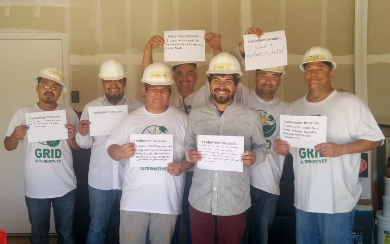 Seven volunteers in hard hats holding signs explaining why they volunteer with GRID Alternatives