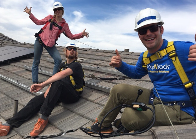 Three workers in safety gear on a rooftop, smiling and giving thumbs up during construction work