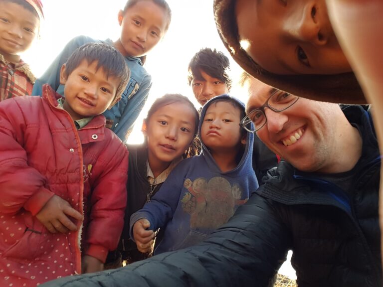 Adult with a group of smiling children gathered together outdoors in Nepal