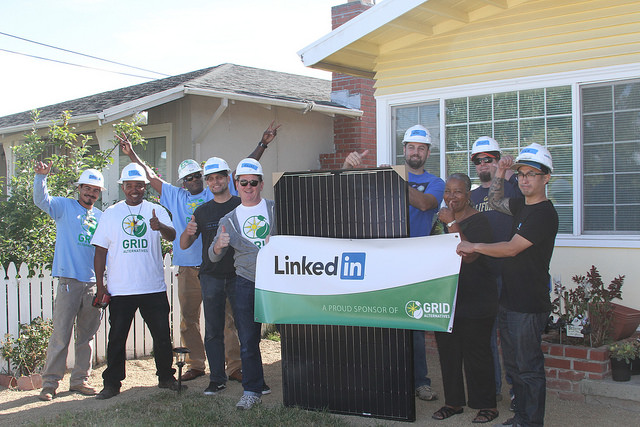 LinkedIn volunteers in hard hats hold a solar panel banner at a residential home installation event