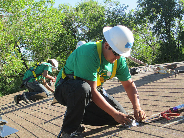 Roofers in safety gear installing solar panels on residential rooftop