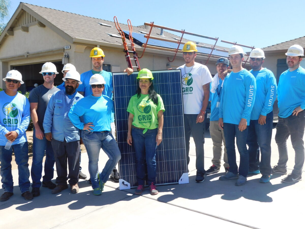 Team of workers in hard hats and blue Sunrun shirts posing with solar panels at a residential installation