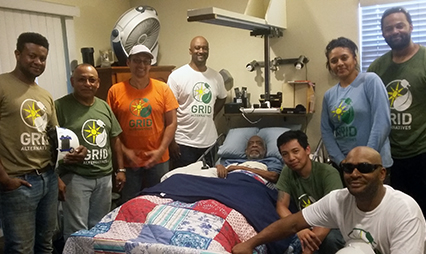 Group of GRID volunteers in matching shirts gathered around a person on a bed, providing support and care