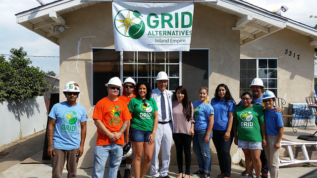 Group of GRID Alternatives staff and participants wearing hard hats and branded shirts stand outside their Inland Empire office building