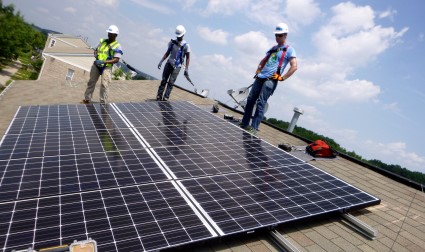 Three workers install solar panels on a residential rooftop under blue sky