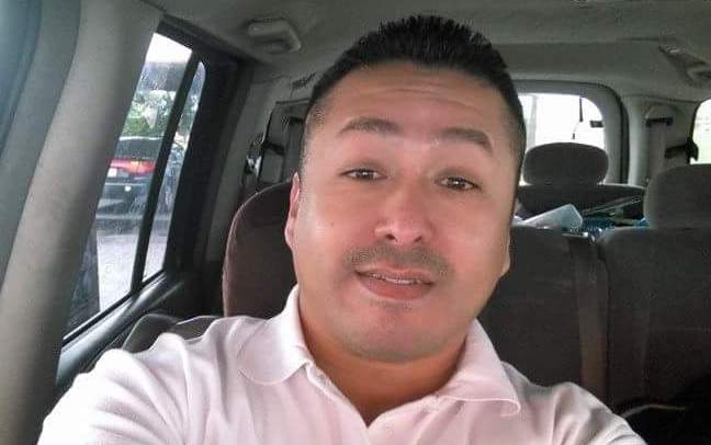 Man in pink shirt sitting in car, smiling at camera