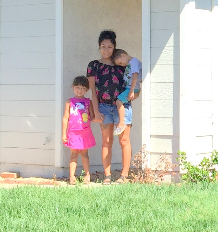 Woman and two children smiling on front porch of house