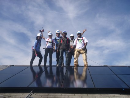Team of solar installers celebrating on rooftop with solar panels beneath them