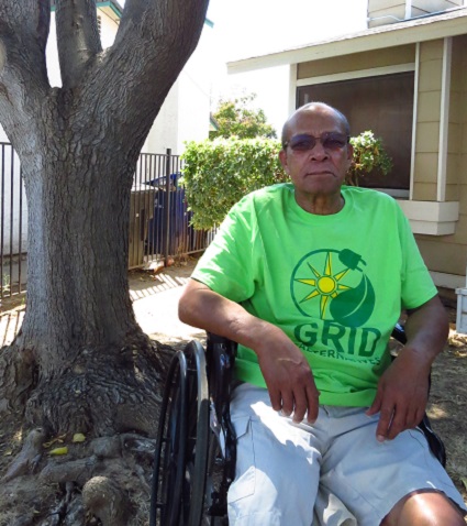 Man in wheelchair wearing green GRID shirt outdoors by large tree