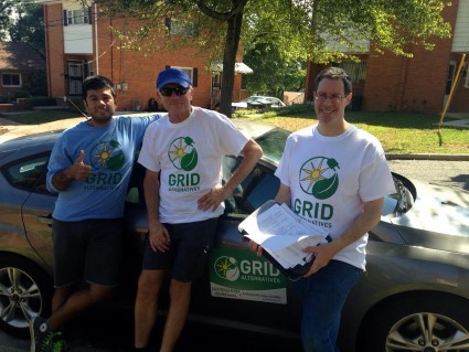 Three people wearing GRID volunteer shirts stand with bikes outdoors